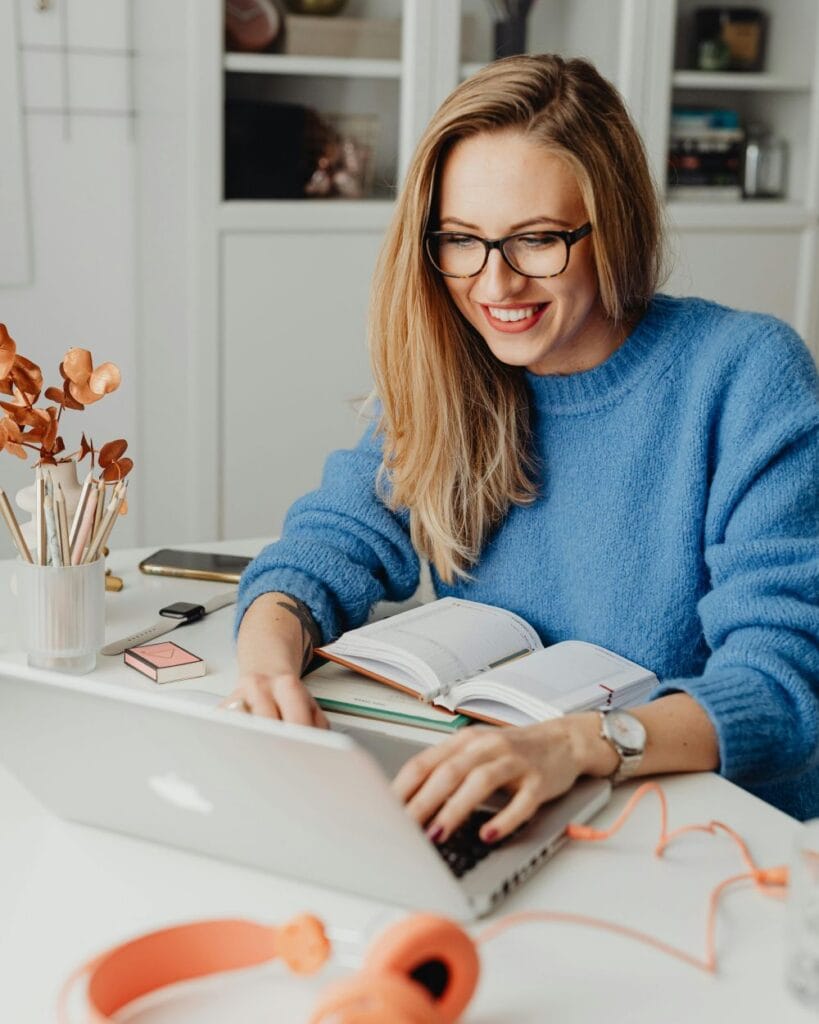A person using her laptop and making notes in a journal