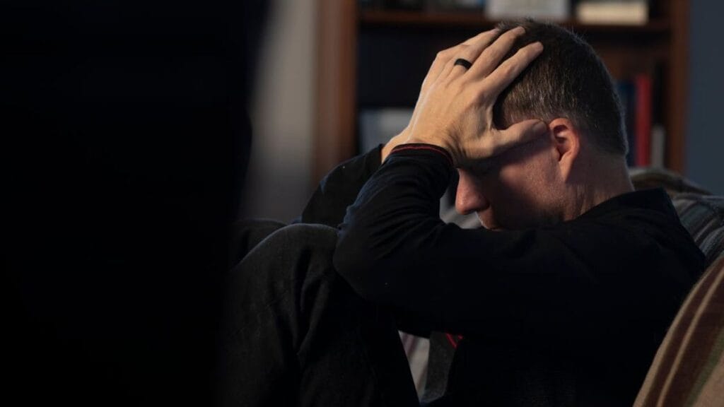 man sitting on a chair holding his head in worry