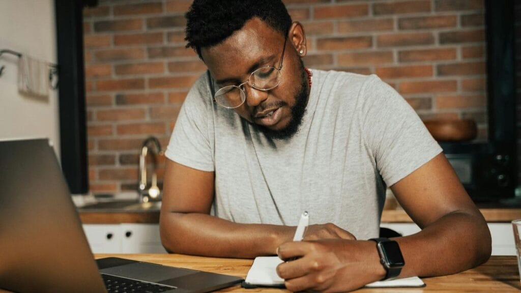 man taking notes during online course.