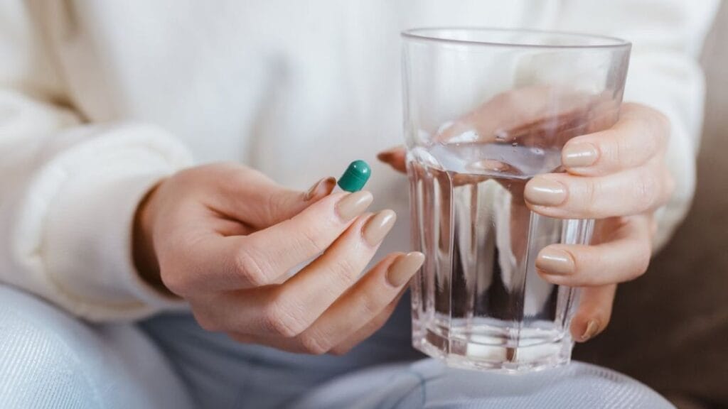 closeup of a person holding a supplement capsule and a glass of water