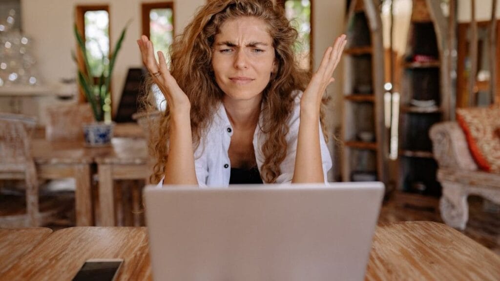 a digital nomad woman showing frustration while sitting in front of her laptop.