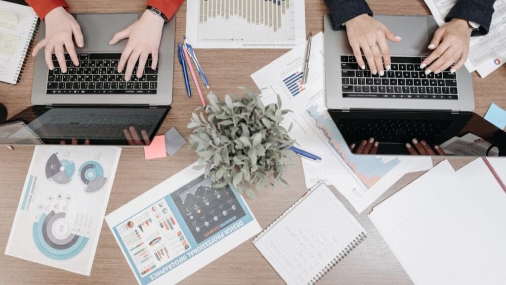 people working on laptops with printouts of data reports on the table.