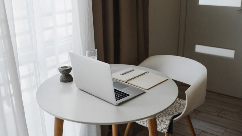 clean small table with laptop and open journal next to a window.