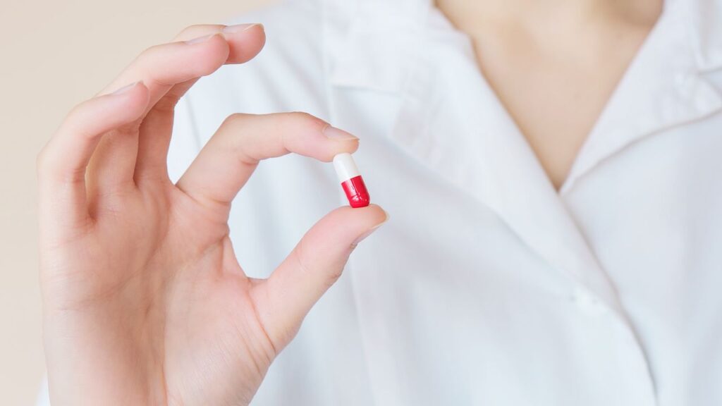 person holding a red and white health supplement capsule